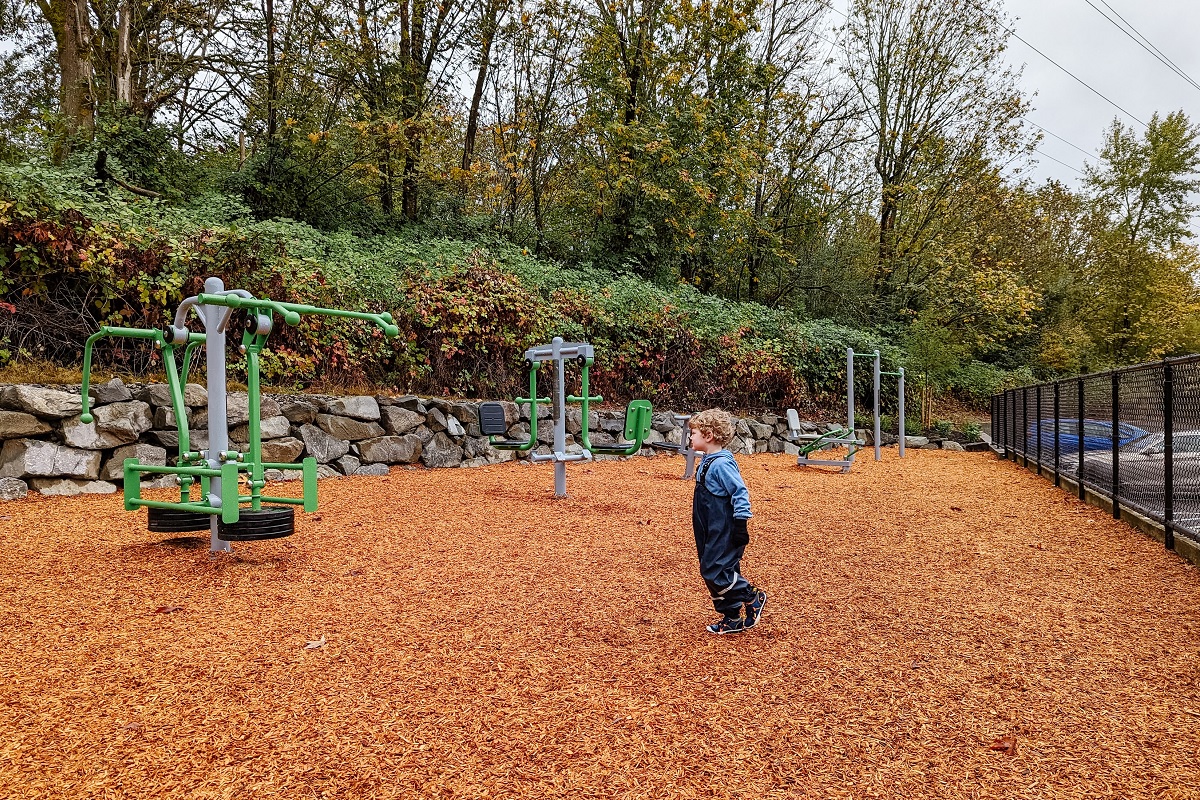 A boys looks at exercise equipment for parents and caregivers adjacent to the new playground at Bellevue’s Newport Hills Woodlawn Park