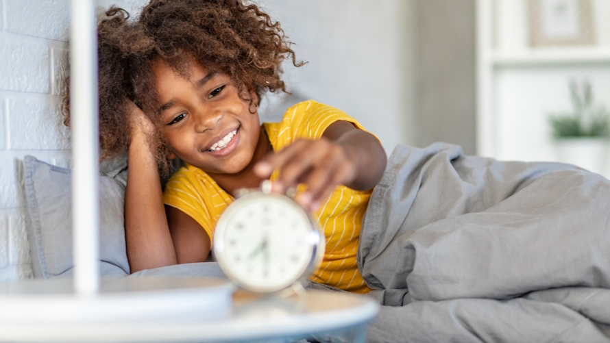 Young girl turning off an alarm clock to help stick to a routine