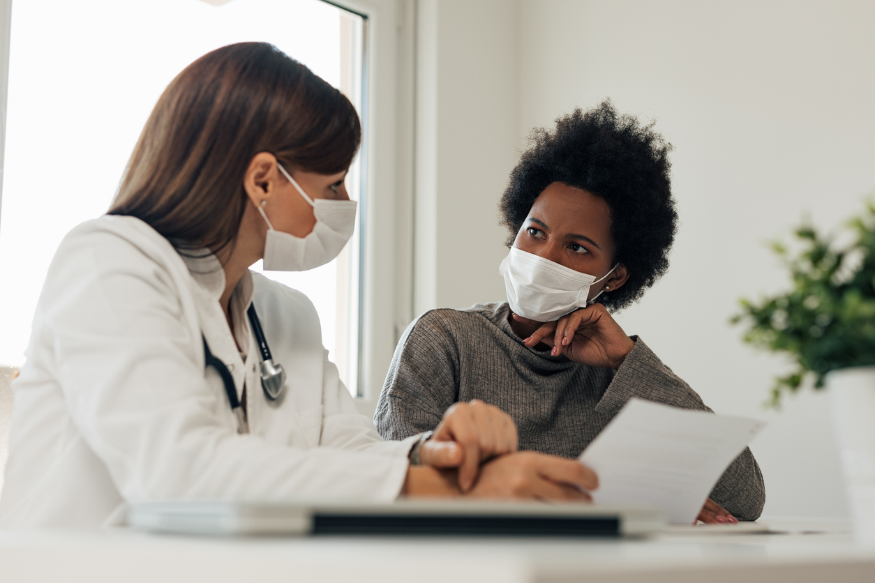 female doctor talking to female patient both wearing masks