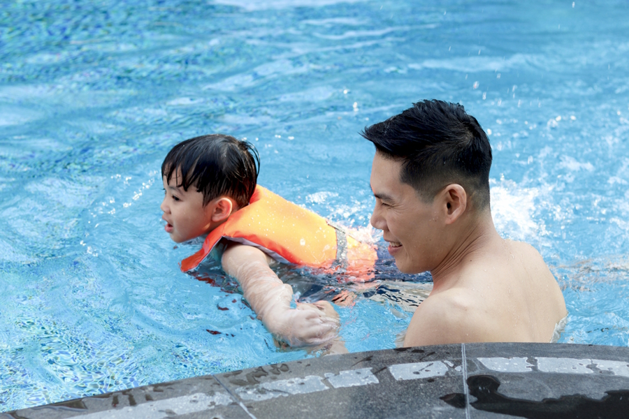 Boy swimming in a pool wearing a life jacket next to his father, water safety for families