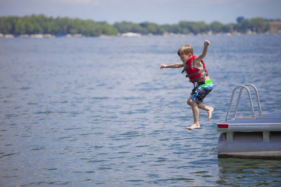 A boy wearing a life jacket jumping off a dock into the water, water safety for families