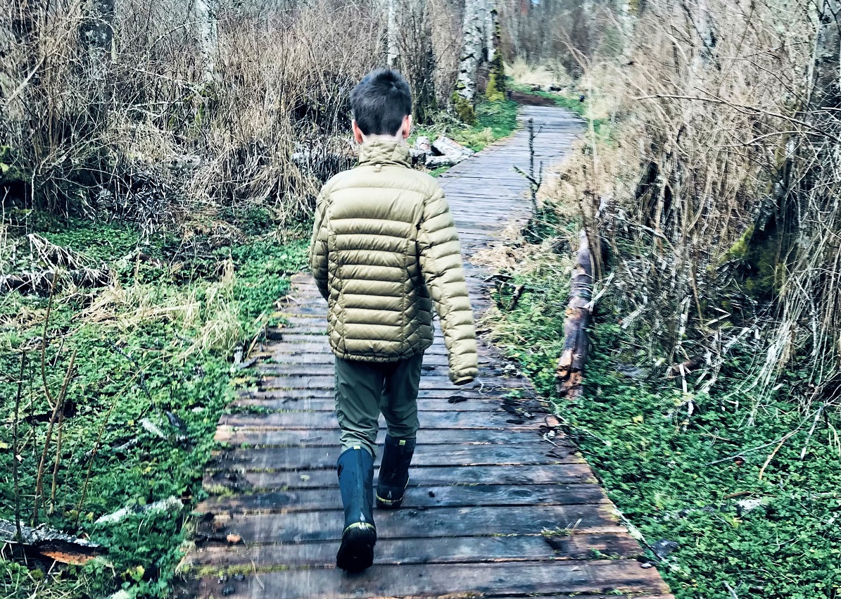 Boy in a green coat hiking along a boardwalk on Whidbey Island, hiking native forest land is among Whidbey's best activities with kids
