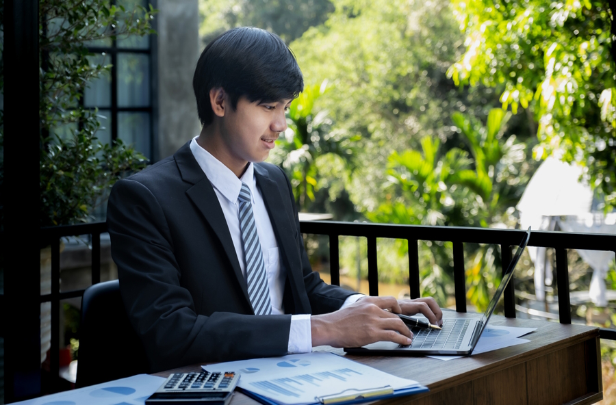 A teen boy wearing a suit working on his computer at a civic leadership opportunity