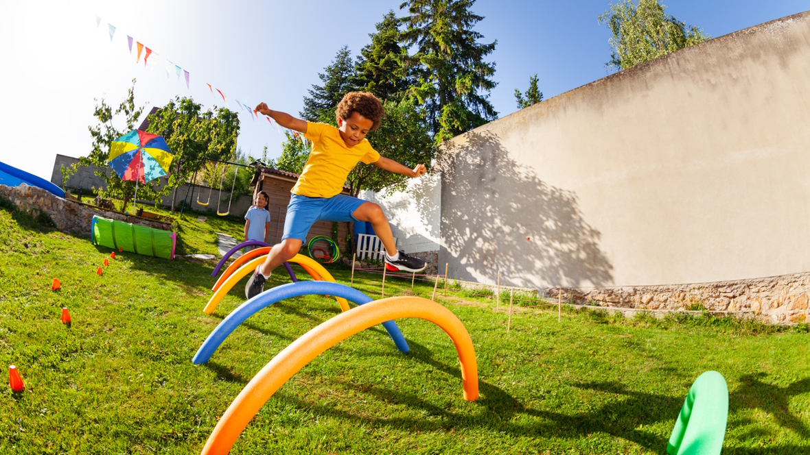 boy jumping over part of an obstacle course outside