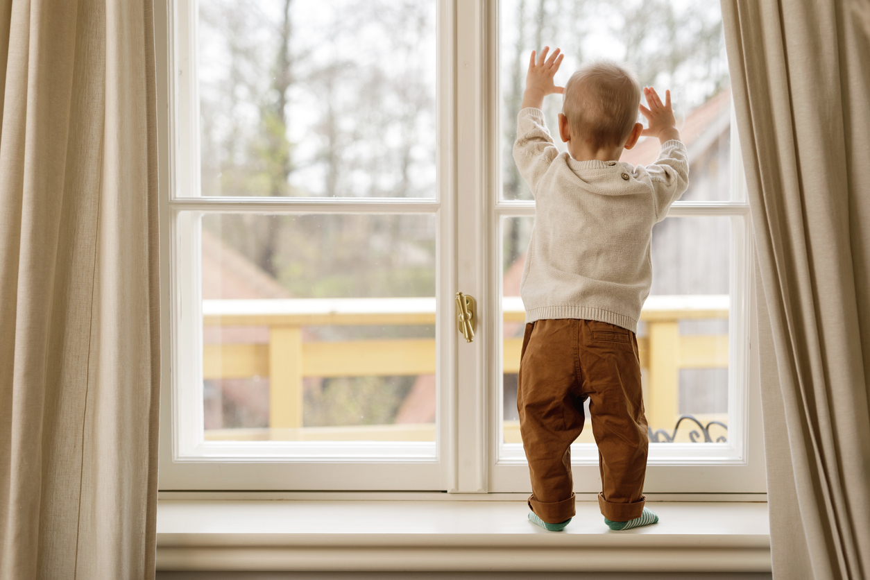 Child standing on a window ledge looking out