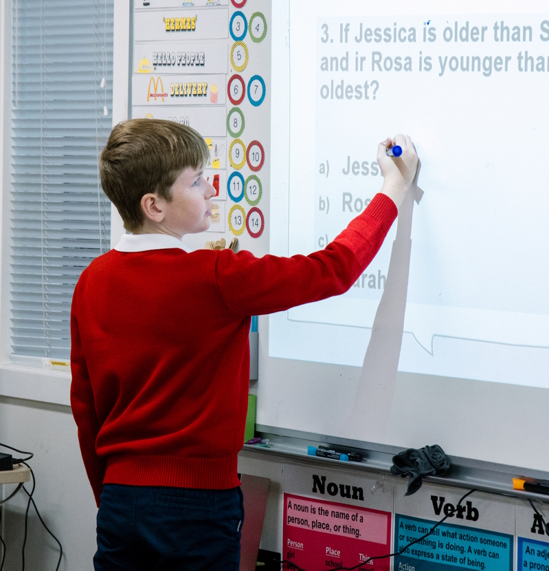 Middle school boy standing at a white board writing and answer to a question