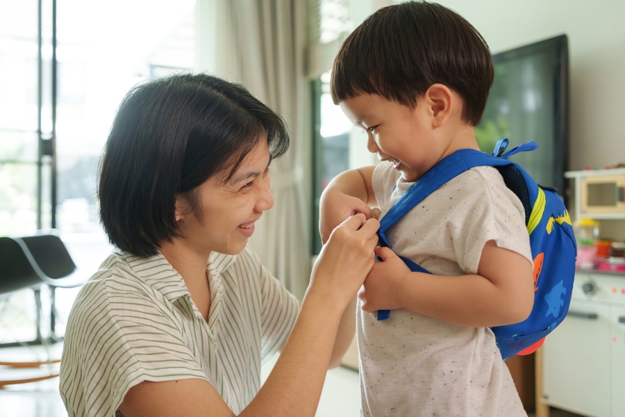mom helping son put on a backpack