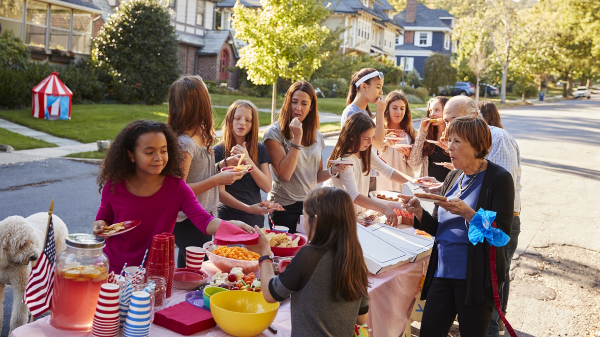 Group of people standing around a table eating food at a neighborhood block party