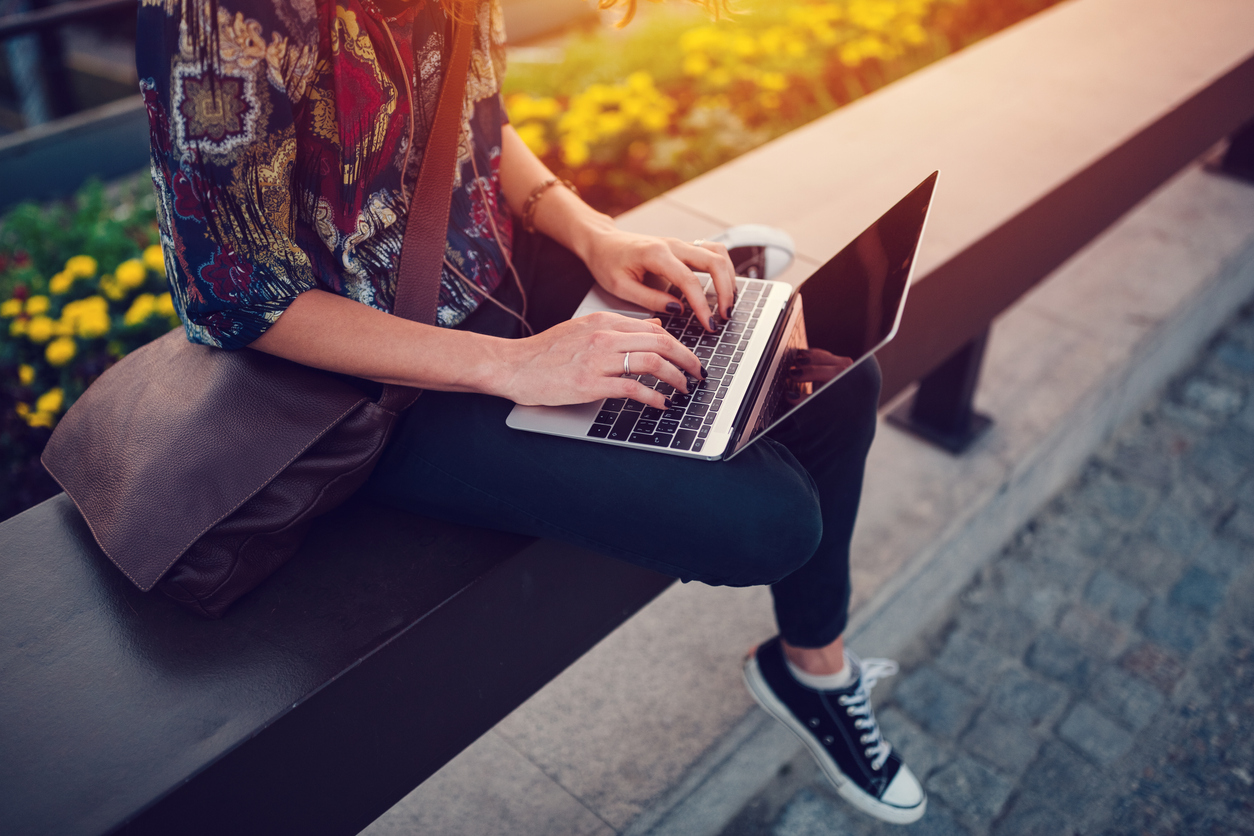 Teenage girl sits outside on a sunny day, working on her laptop