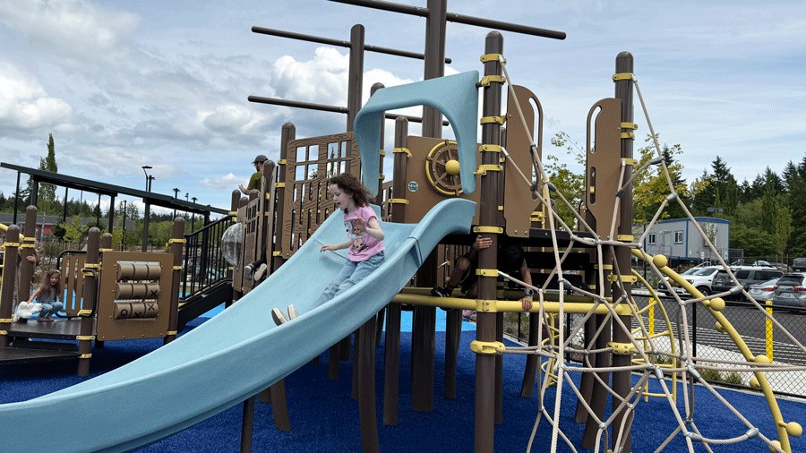 girl sliding down a blue slide at Doris Heritage Park playground in Gig Harbor