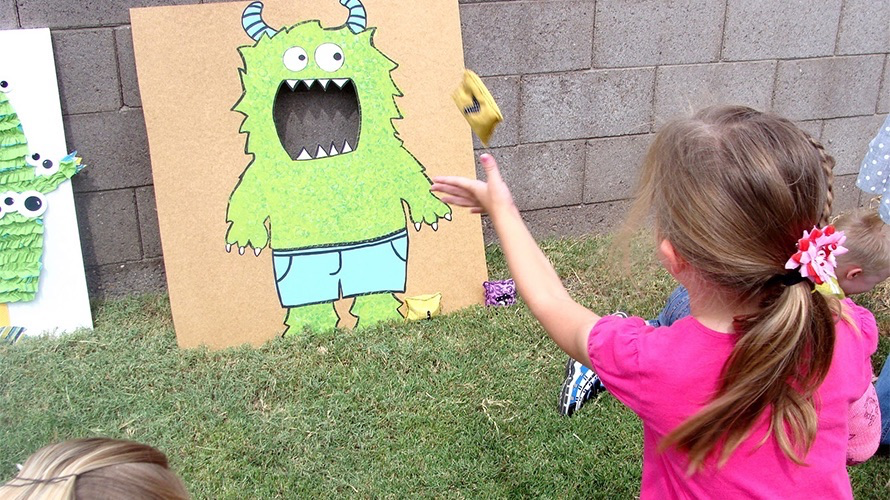 girl throws a bean bag into the mouth of a green monster while playing a Halloween party games for kids