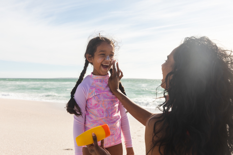 Girl on the beach having sunscreen put on her face in the summer