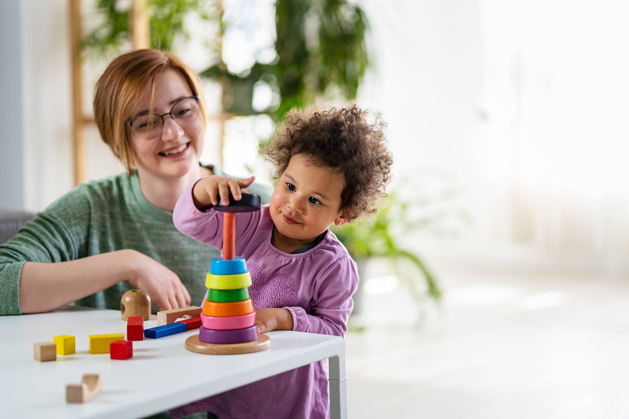 Nanny looking at a child who is playing with an educational didactic toy