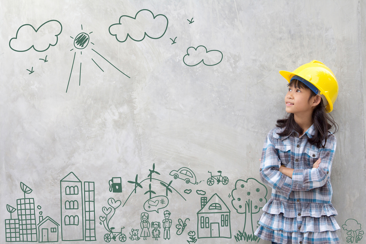 girl in a yellow hardhat standing against a wall with a cityscape drawn on it