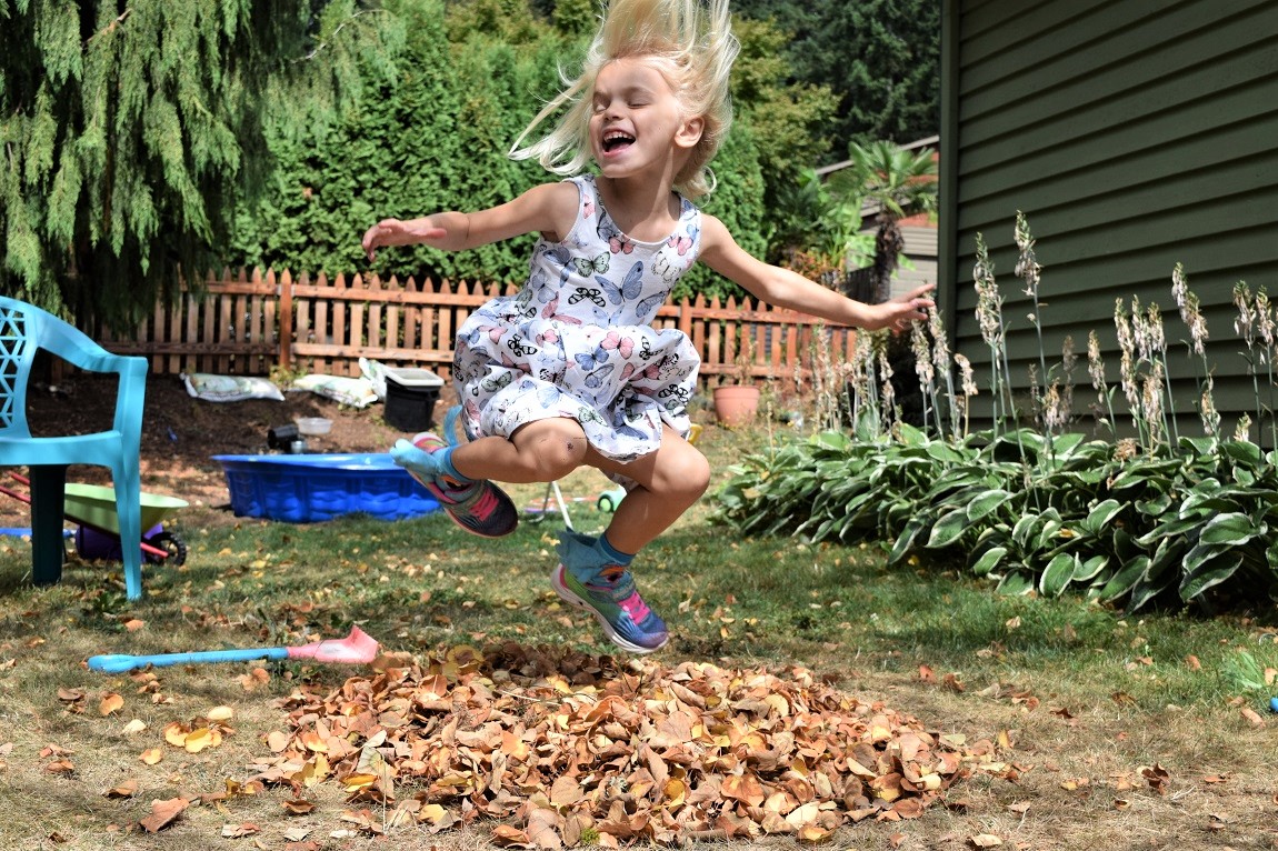 Girl jumping happily in a pile of leaves in her yard can outdoor time raise your happiness ranking