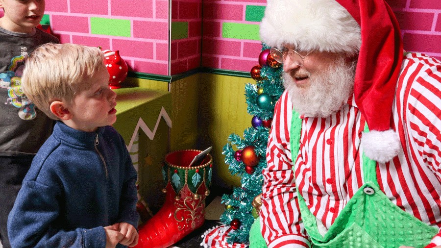 Santa listening to a child at Kringle's Inventionasium experience, an immersive attraction in Seattle for families during Christmas