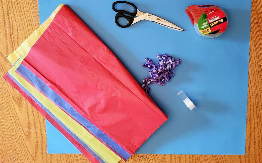 Blue paper, scissors, tape and multi-color tissue paper which will be used to make a back to school boy sitting on the sidewalk with a blue backpack holding a yellow back-to-school Schultuete