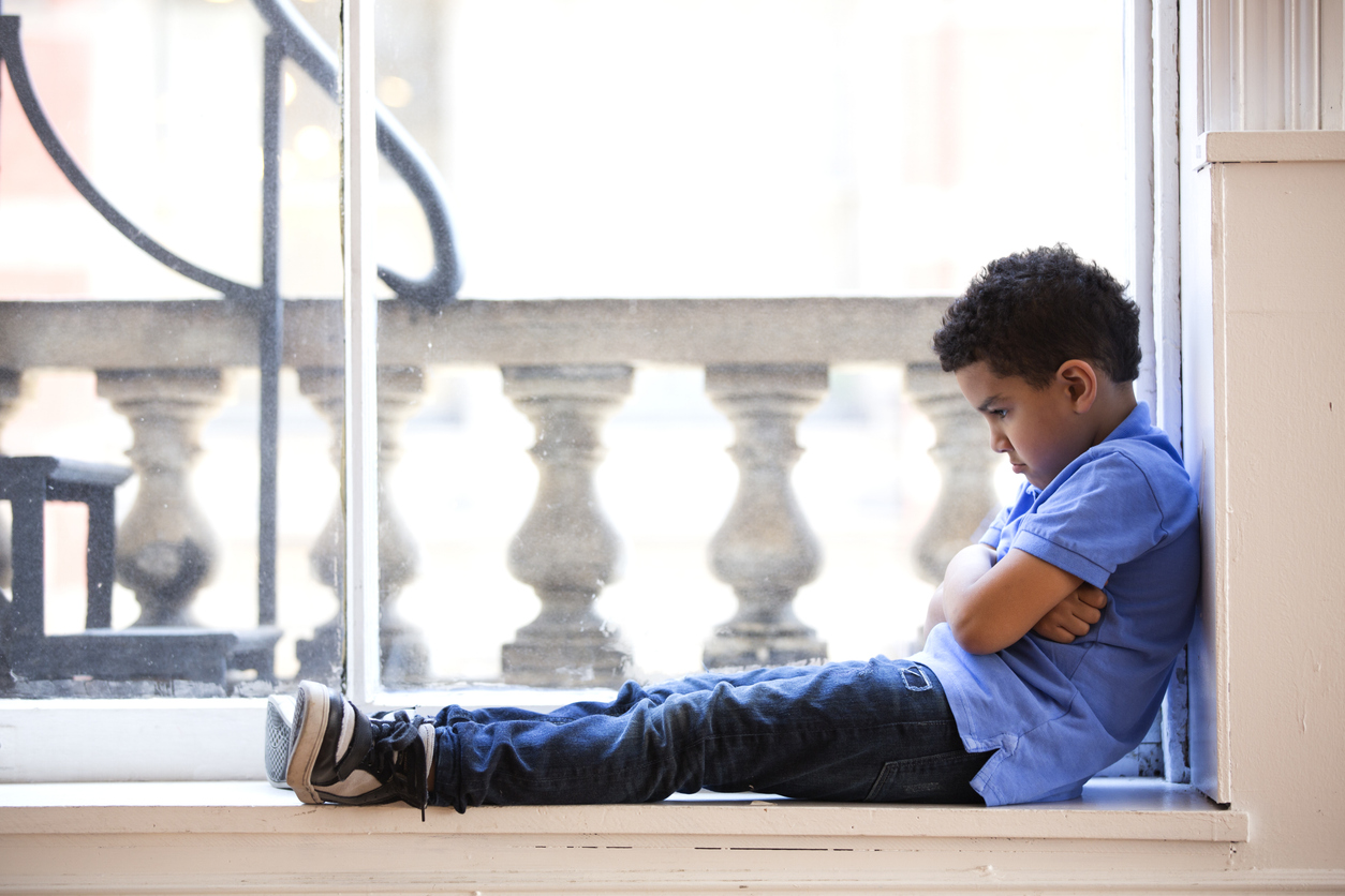 a child sits in a window looking defeated and helpless