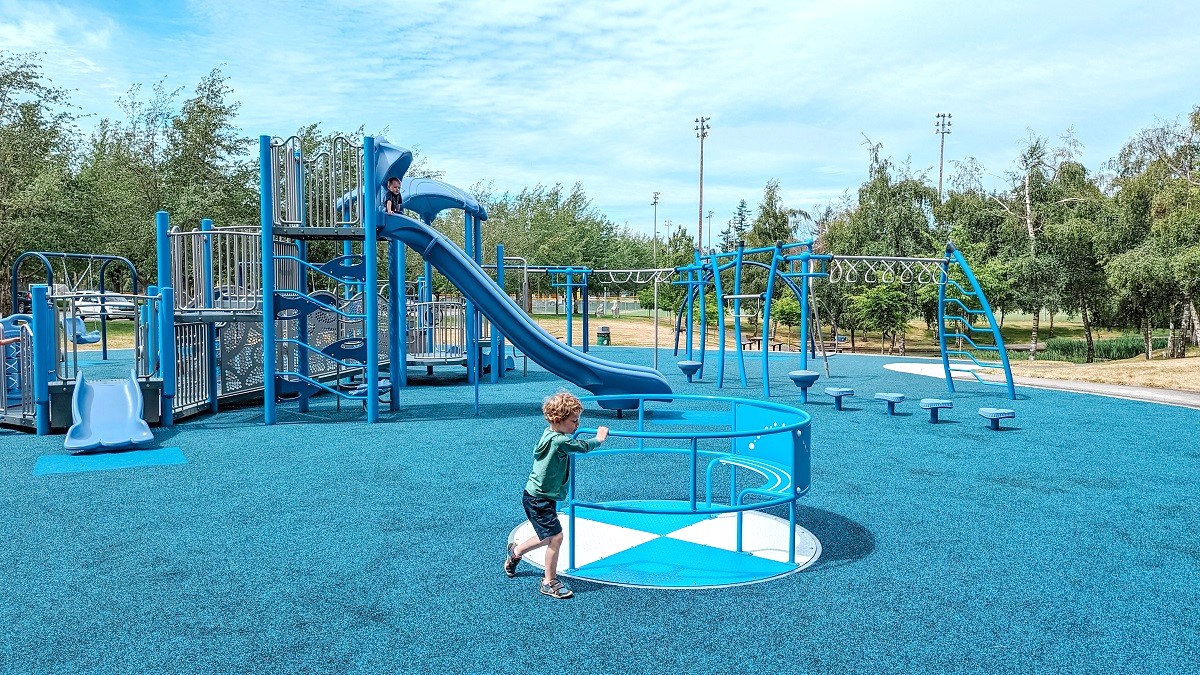 Kids play on a level-entry merry-go-round spinner at the inclusive new playground at Meadowdale Playfields in Lynnwood, Washington, near Seattle
