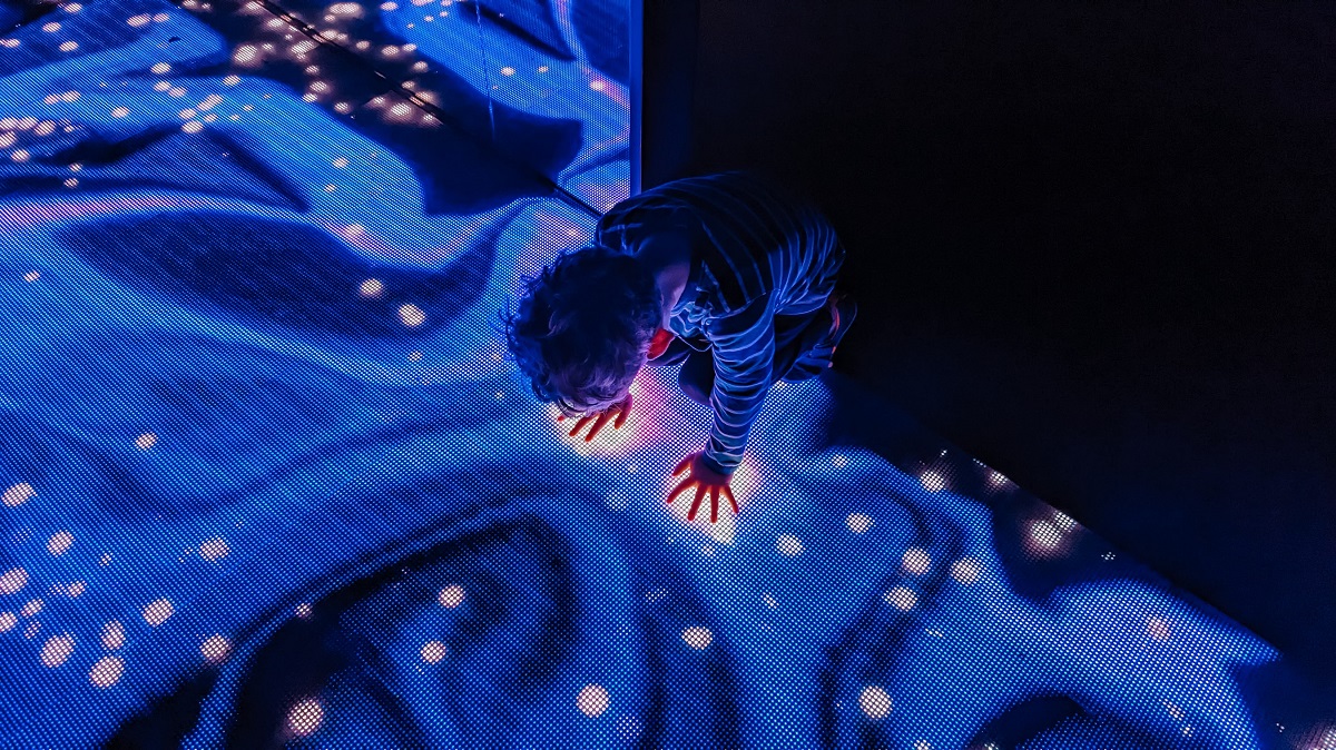 A young boy crouches on the floor in a light room interactive display at Seattle's new WNDR Museum