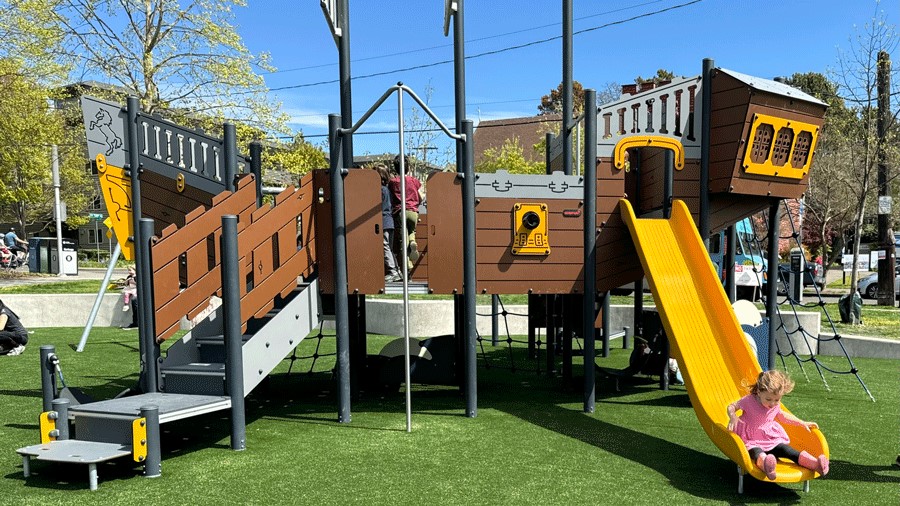 A girl slides down a yellow slide at the newly opened Ballard Commons playground in Seattle