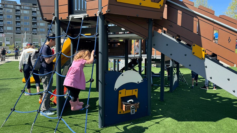A girl climbs a rope ladder on a sunny day at the recently opened Ballard Commons Playground