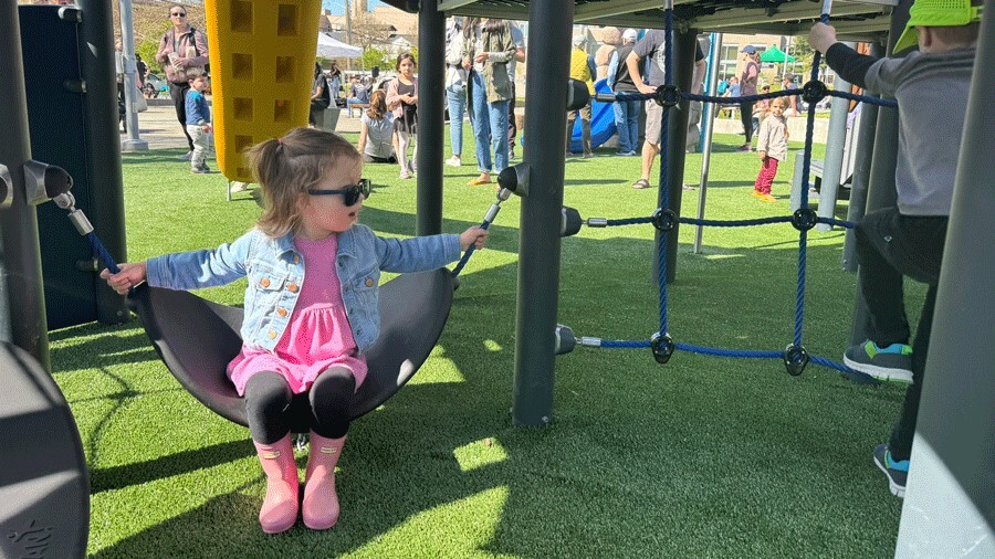 Small child swinging underneath the ship at new Ballard Commons Park playground in Seattle