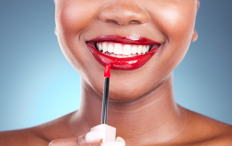 smiling woman putting on red lip gloss