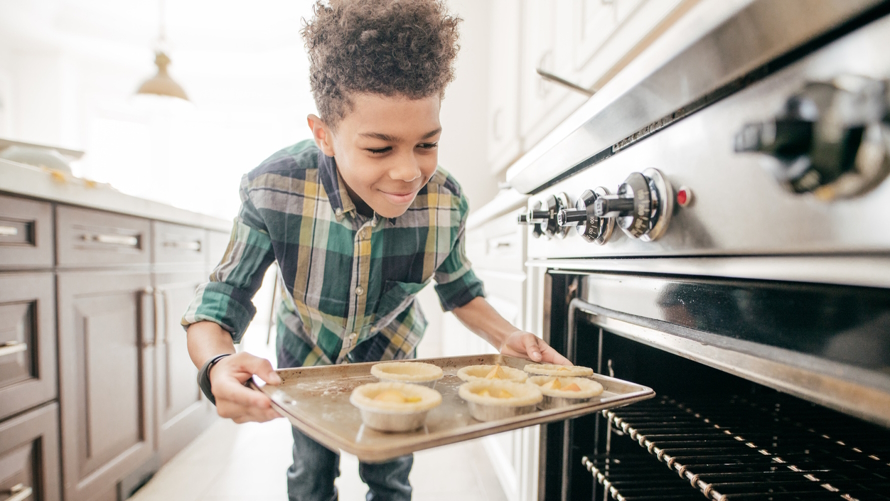 boy baking and putting small pies in the oven