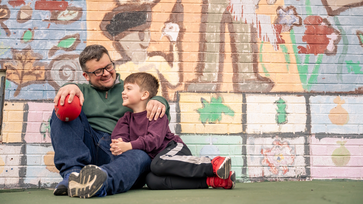 dad and son sitting together outside in front of a mural