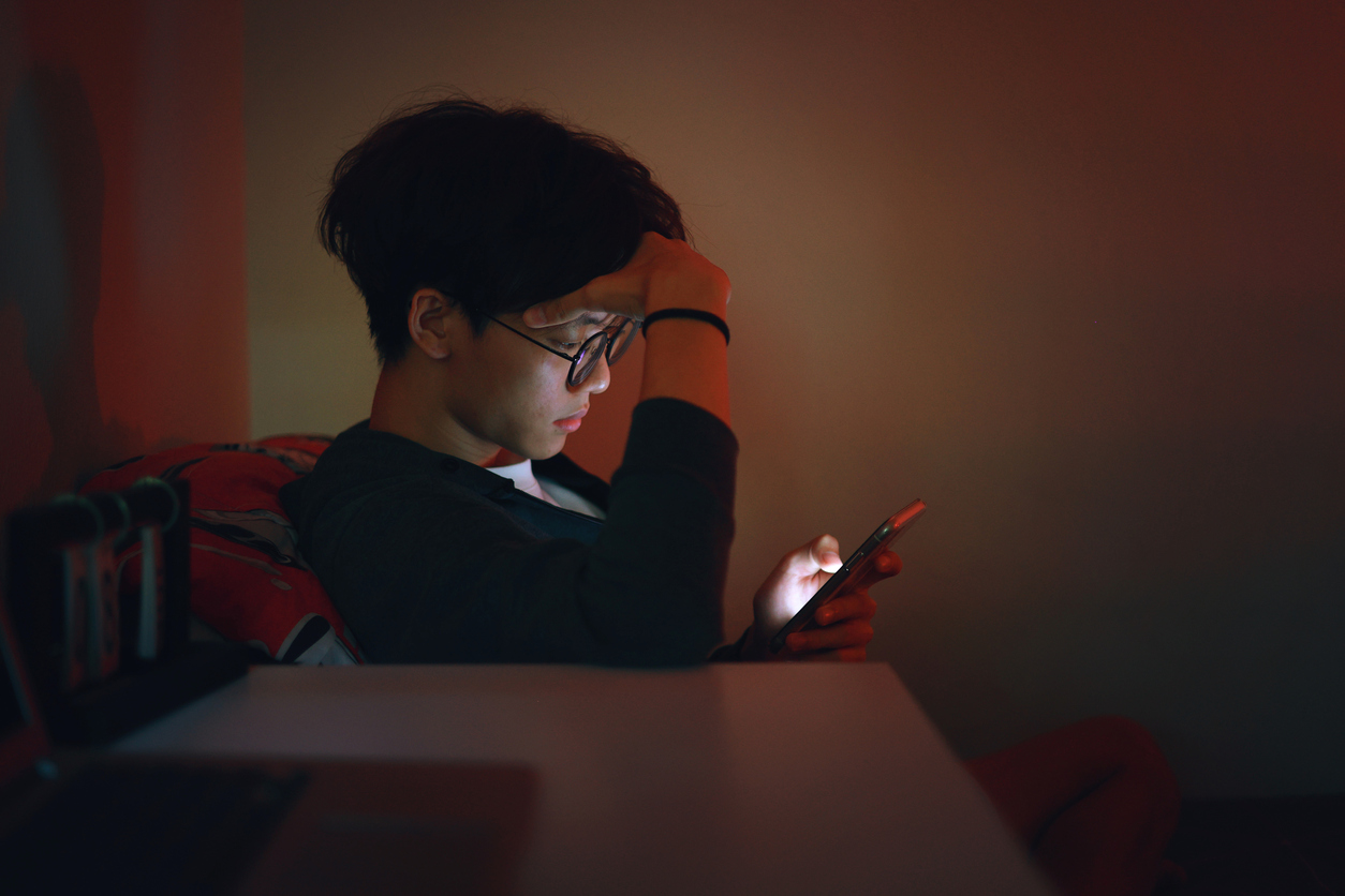 teen seemed stressed while looking at his phone in a dark room