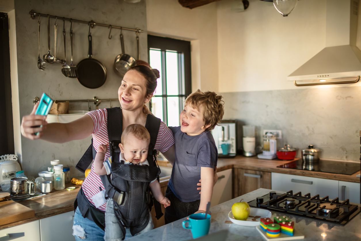 mom shoots a video with her phone in a kitchen with two kids