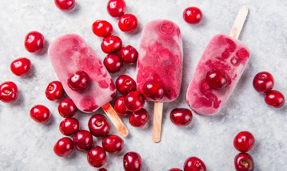 Cherry popsicles lying on a table with cherries all around them are a great summertime treat