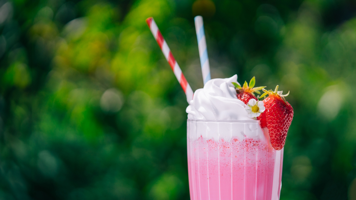 Strawberry soda float in a glass with two straws and a whole strawberry and a flower on the top
