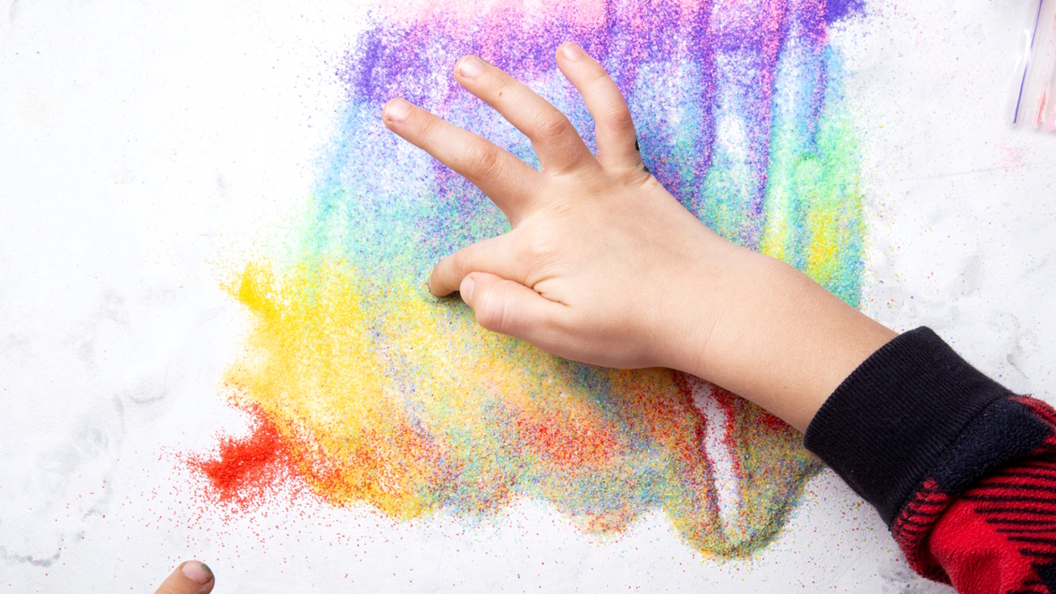child's hand making a design with colored salt