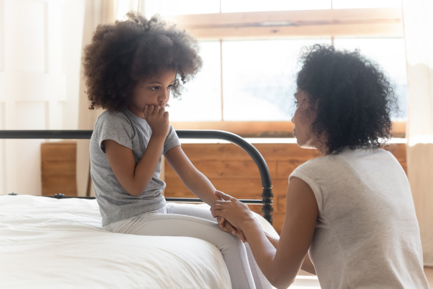 Young girl looking shy and sitting on a bed holding hands with a mother