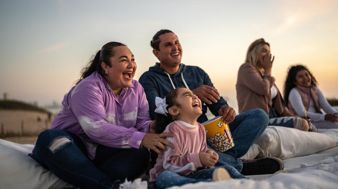 Family on a blanket with popcorn, using outdoor gear for a summer movie