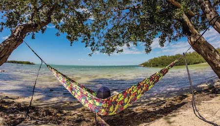 A person relaxes on the beach in a camo ENO hammock.