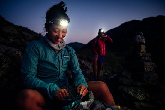 A woman smiles outside at night wearing a PETZL headlamp.