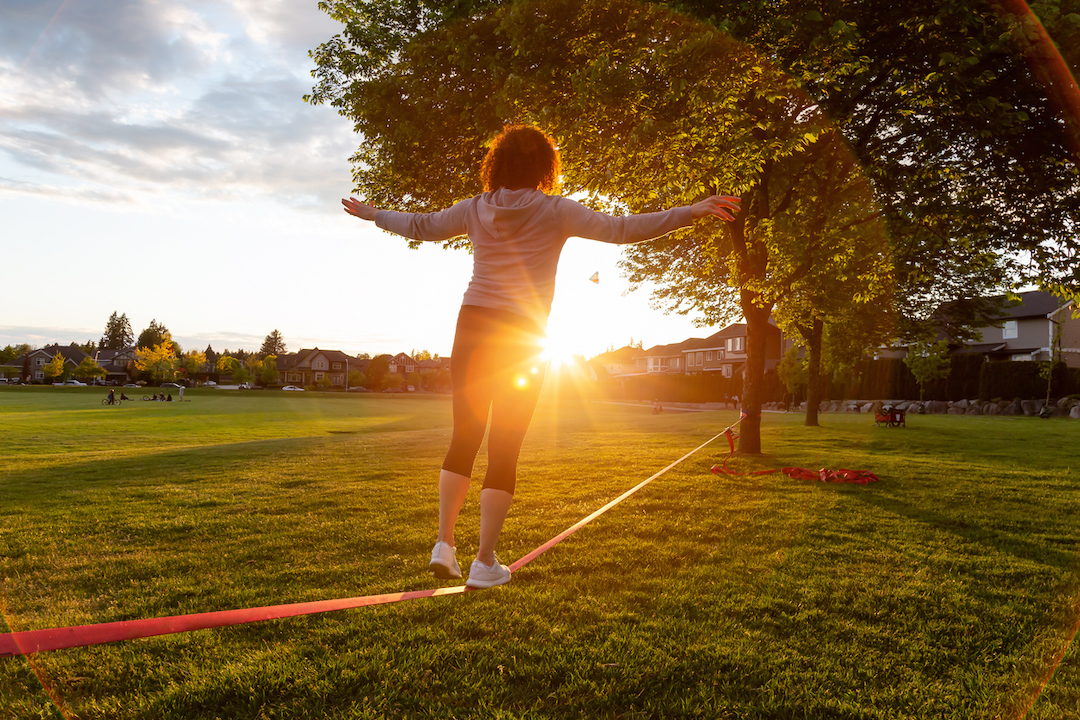 Back view of a person walking on a slackline with the sun setting.
