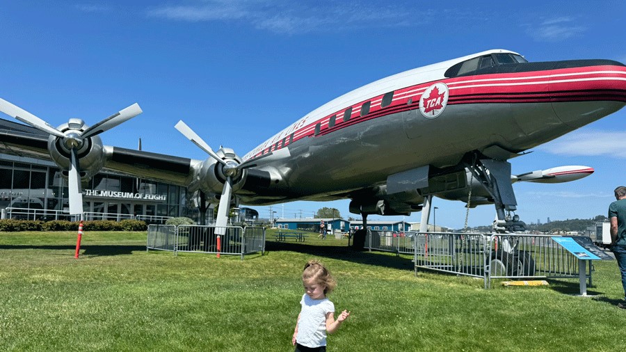 Young girl at the entrance of The Museum of Flight, a Seattle attraction, with a large airplane on the front lawn