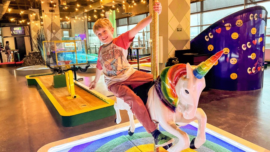 young child at putt putt mini golf course with a unicorn near Seattle on a rainy day, an indoor activity for families