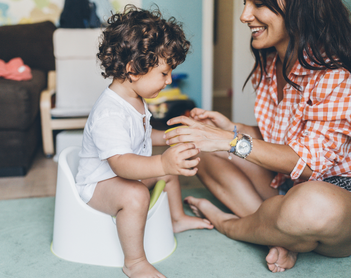 Mom sitting on the floor next to a baby sitting on a baby potty