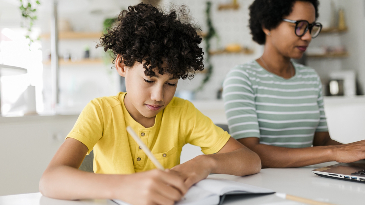 boy doing homework with mom sitting nearby working
