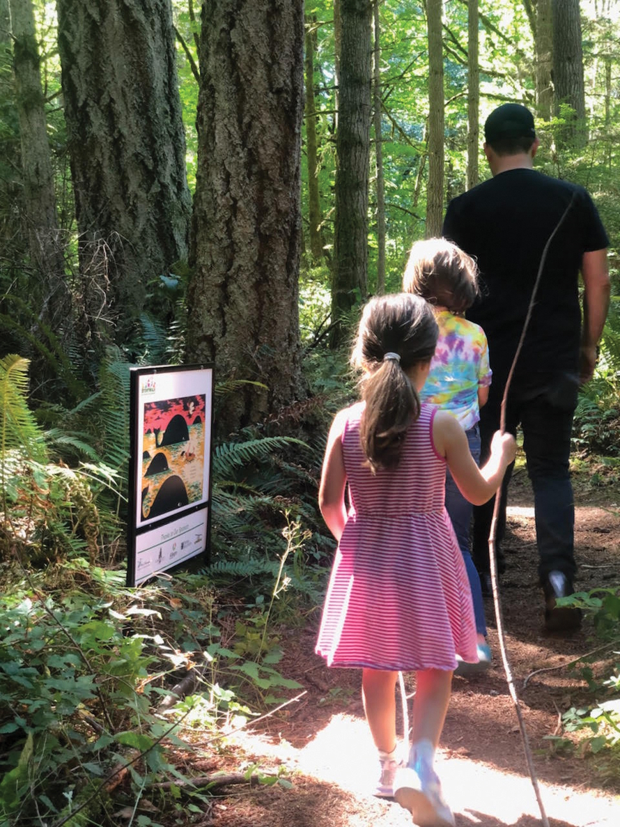 Two children and one adult walking in the woods. popupstorywalk.org