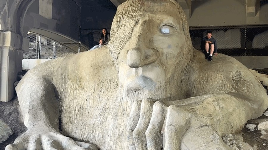 Fremont troll statue sits under Seattle's Aurora Bridge in the Fremont neighborhood, boy posing for photo while people look on best instagram sights in seattle