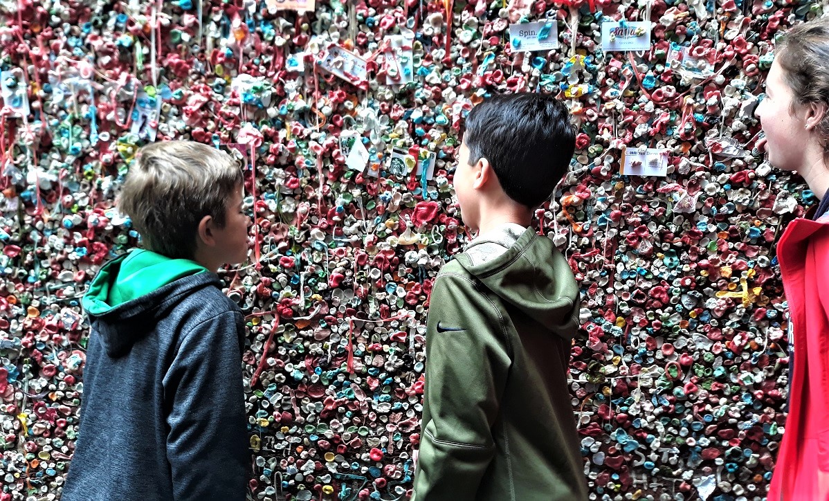 Tweens and teens stick their tongues out toward the Pike Place Market Gum Wall best instagram landmarks around Seattle