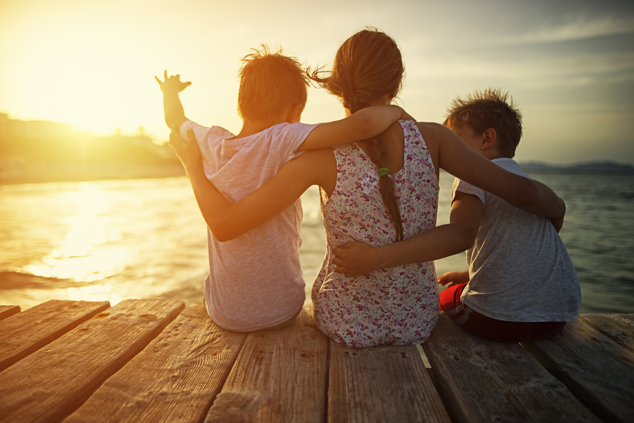 mother with sons sitting on either side of her on a dock at sunset