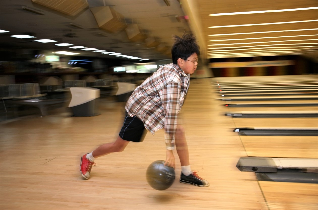 Boy in plaid shirt and short bowling at bowling alley near Seattle Kids Bowl Free program Seattle area kids families