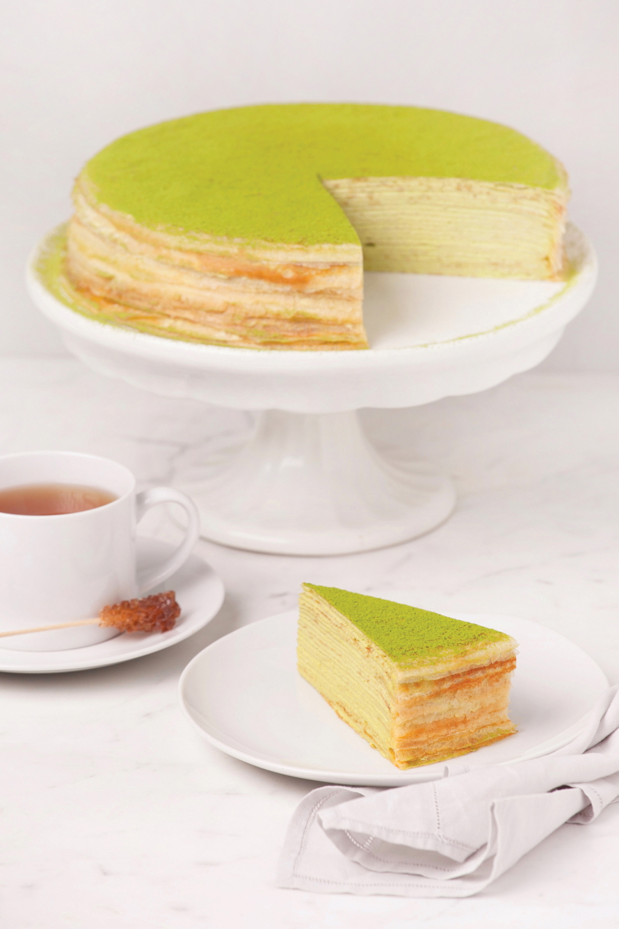 Layer green tea cake with slice cut out and sitting on a white plate